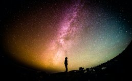 a silhouette of a person looks up at the Milky Way at night