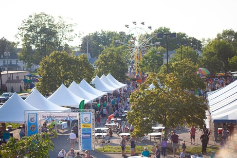a wide shot of tents in the foreground lead to a ferris wheel and other rides in the background