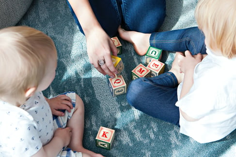 two children sit on the floor, playing blocks with their mom