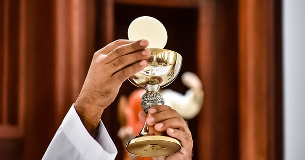 Hands holding holy eucharist and chalice aloft